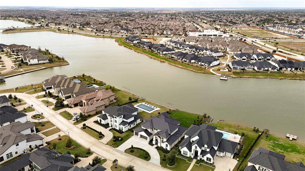 This aerial photo showcases a serene, upscale lakeside neighborhood with spacious modern homes, well-maintained lawns, and scenic water views. Ideal for those seeking a tranquil, community-oriented environment.