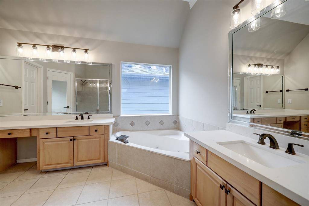 [Primary en-suite bathroom] The centerpiece of the bathroom is a jetted bathtub, nestled beneath a large window that allows natural light to bathe the space during the day. On either side of the room, you'll find two elegant vanities, each with its own sink and mirror. Standing shower and water room opposite side