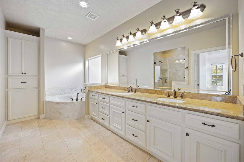 Luxurious & spacious primary bedroom with elegant tray ceiling and ceiling fan. Features rich hardwood floors, French doors leading to a balcony, and ample natural light from multiple windows.