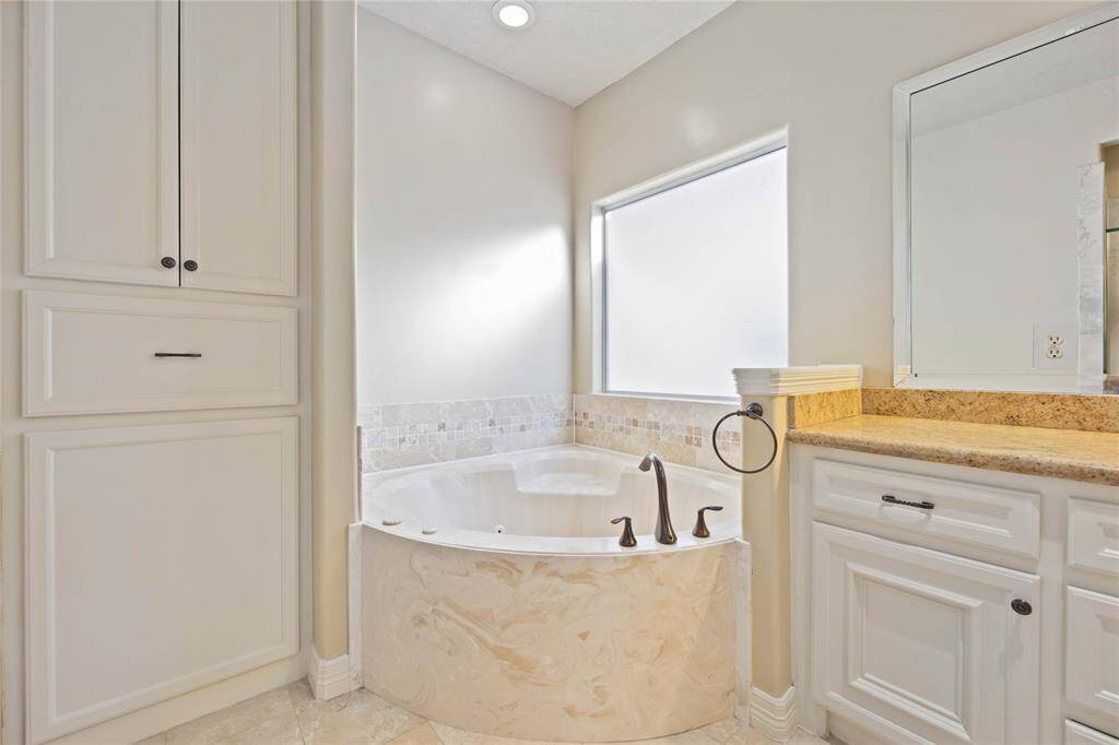 Primary ensuite featuring a large dual-sink vanity with ample storage, elegant lighting, a luxurious soaking tub, and a glass-enclosed shower.