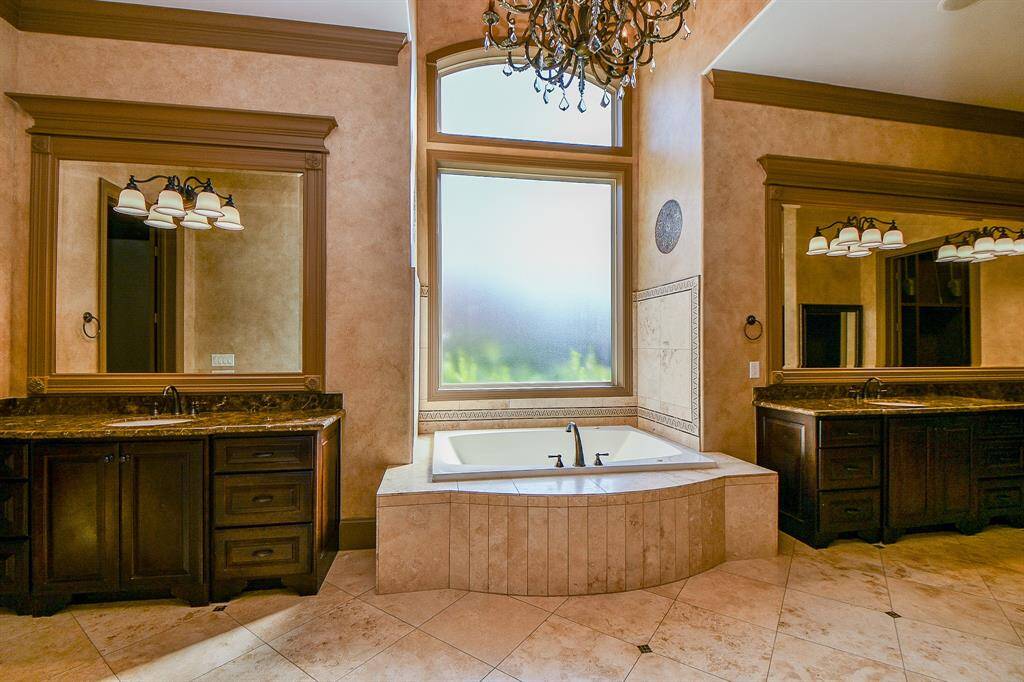 This is a spacious primary bedroom walk-in closet with ample built-in shelves, drawers, and hanging rods for organized storage. A central island provides additional countertop space for accessories or folding clothes. The closet is well-lit with several light fixtures.