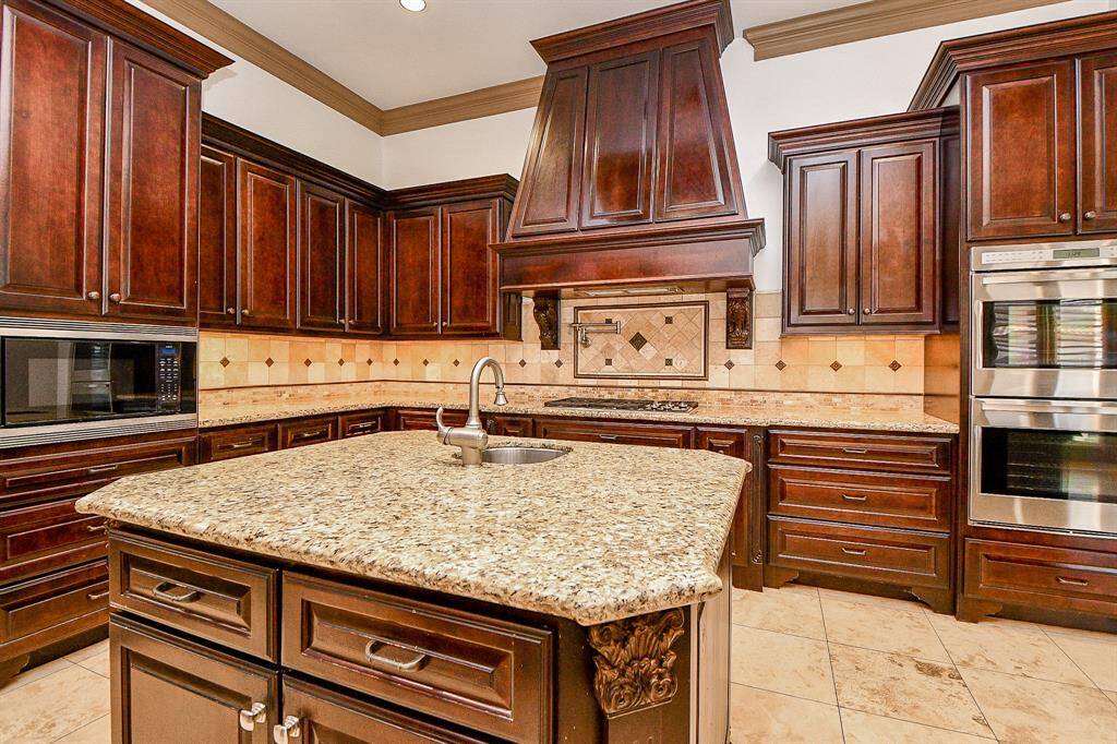 This is a spacious kitchen featuring rich, dark wood cabinetry, granite countertops, a central island, and modern, stainless steel appliances.