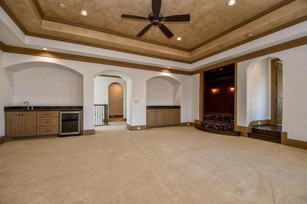 This is a spacious Gameroom featuring a tray ceiling with recessed lighting and a ceiling fan, arched doorways, a built-in wet bar with a wine fridge. The room is carpeted and has ample space for versatile furniture arrangements.