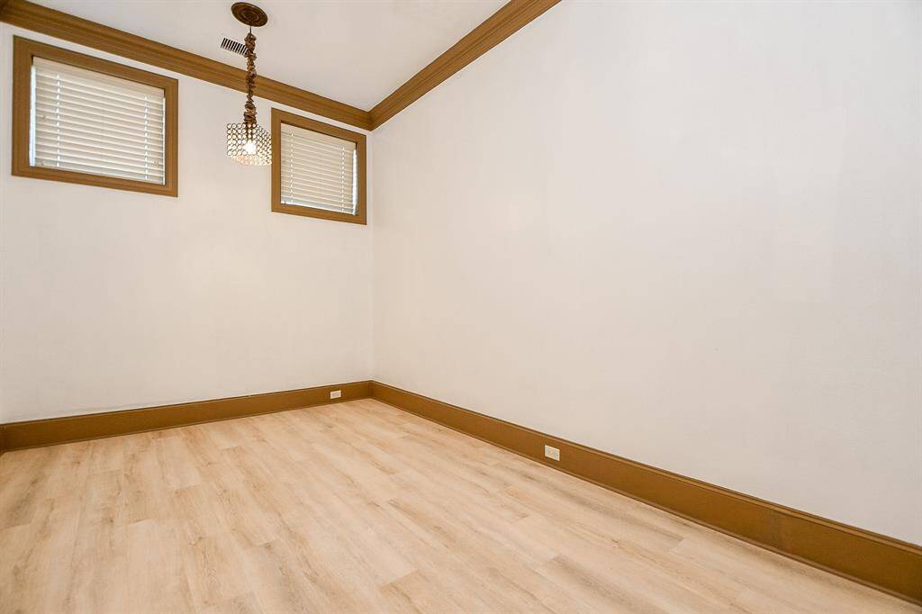 This is a clean, empty room featuring light wooden flooring, two windows with blinds, and a decorative ceiling light fixture. The room has a neutral color scheme with white walls and brown trim.