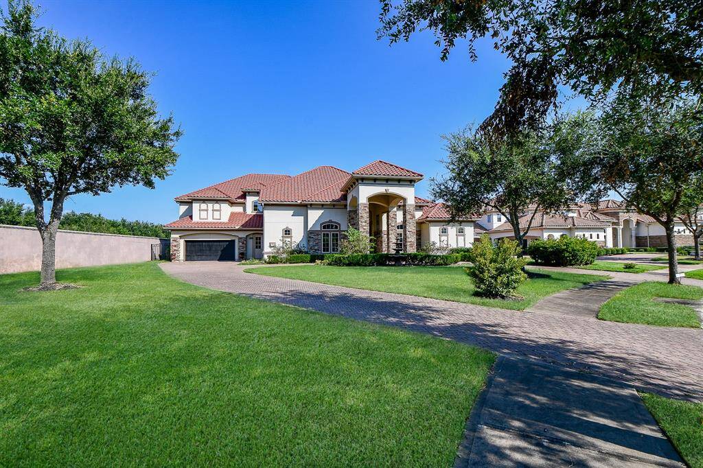 This is a spacious, single-family home featuring a Mediterranean style with a red-tile roof, an arched entryway, and a four-car garage. The property includes well-manicured lawns and mature trees, offering an inviting suburban atmosphere.