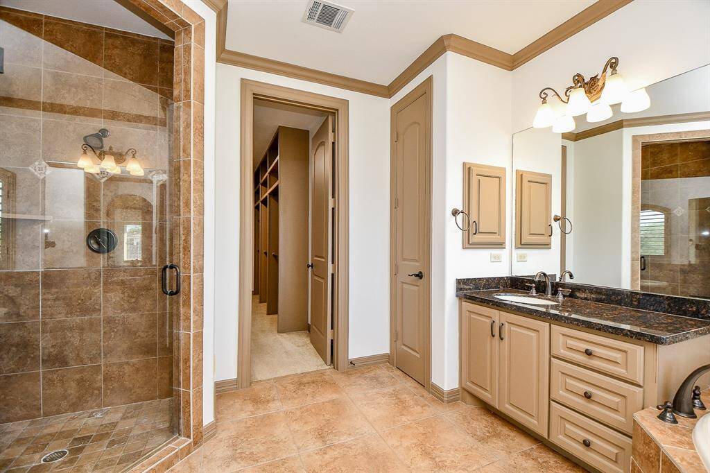 This is another view of the spacious second primary bathroom upstairs featuring a walk-in shower with glass enclosure, a large vanity with dual sinks and granite countertops, and ample cabinet space. The room is finished with tile flooring and has a neutral color scheme.