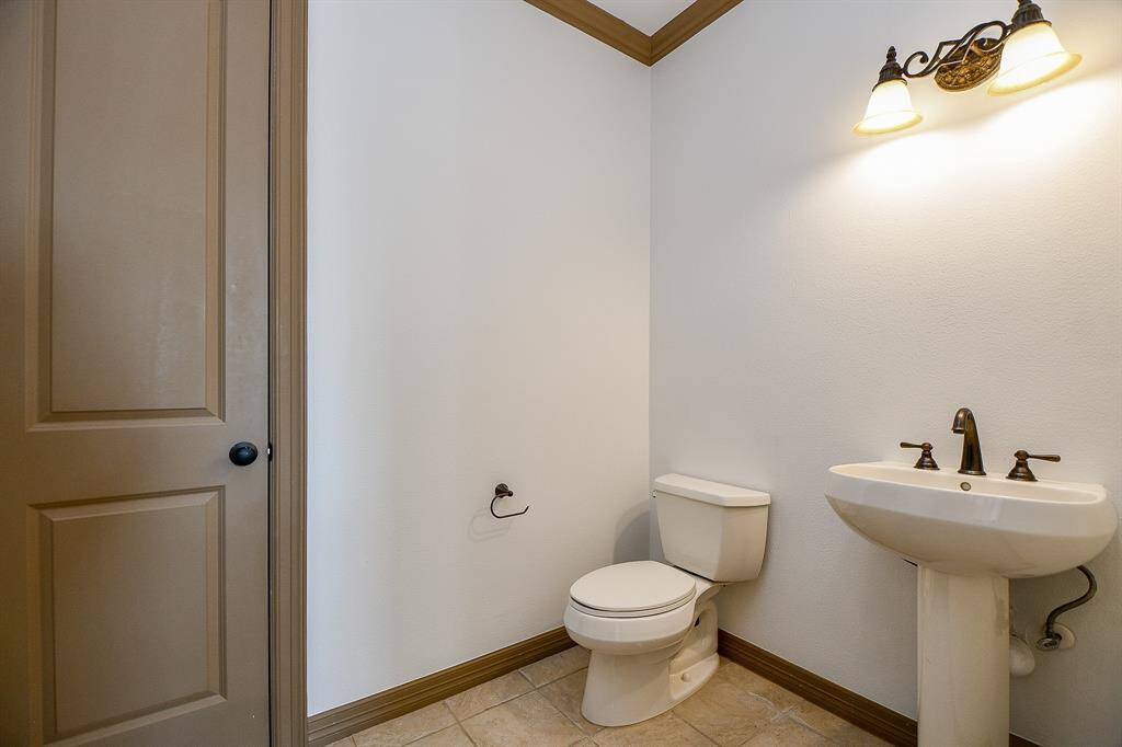 This is a compact half-bathroom featuring a toilet and pedestal sink, with warm lighting and neutral tones.