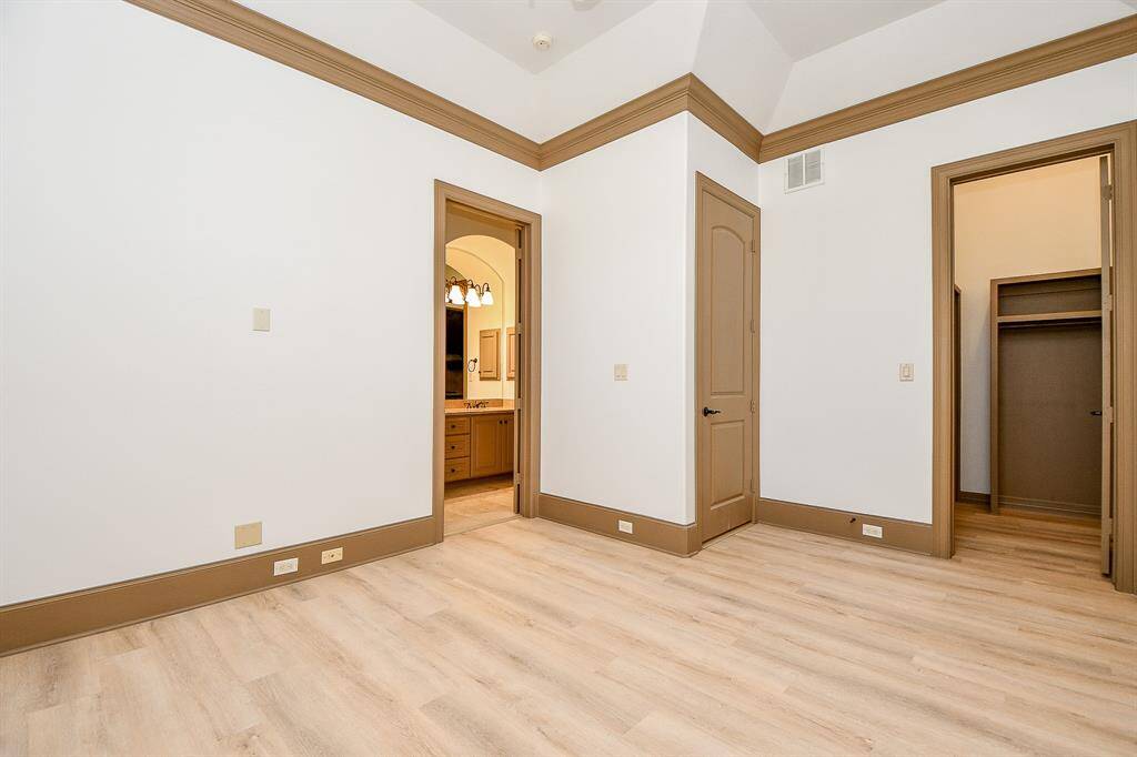 This is a spacious, well-lit bedroom with neutral carpeting, a vaulted ceiling with a fan, two windows providing natural light, and a large closet.