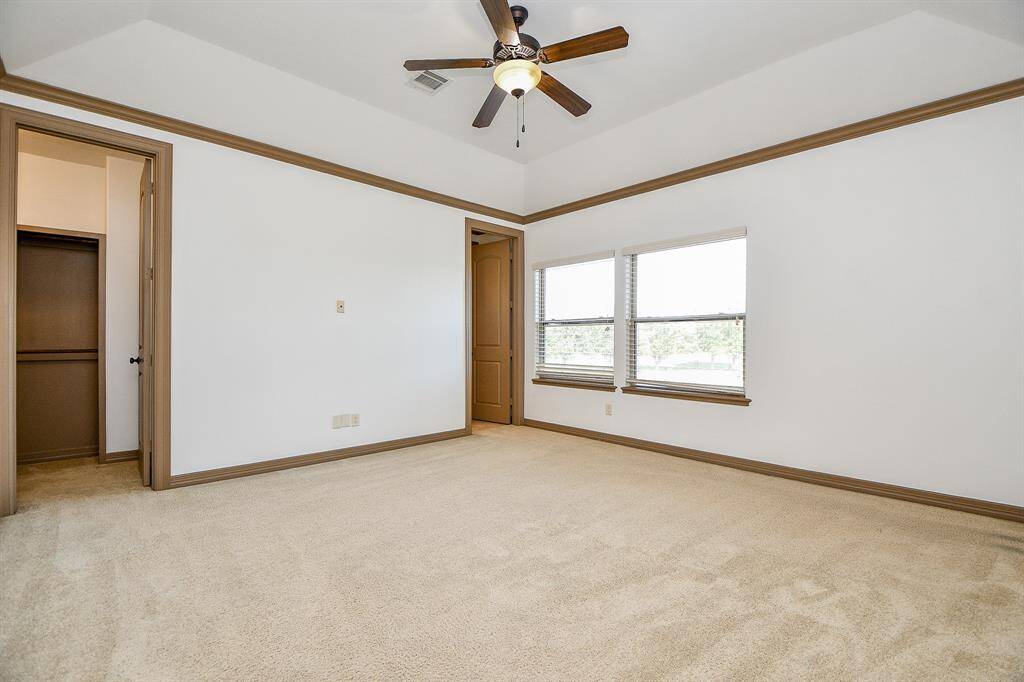 This is a spacious, well-lit bedroom with neutral carpeting, a vaulted ceiling with a fan, two windows providing natural light, and a large closet.