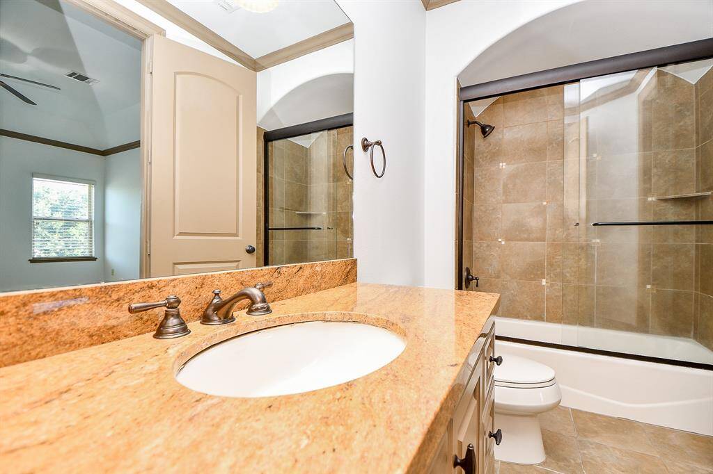This is a modern bathroom featuring a granite countertop with a built-in sink, bronze fixtures, a large mirror, a walk-in shower with glass doors, a separate tub, and a toilet. The room has a neutral color palette and a window providing natural light.
