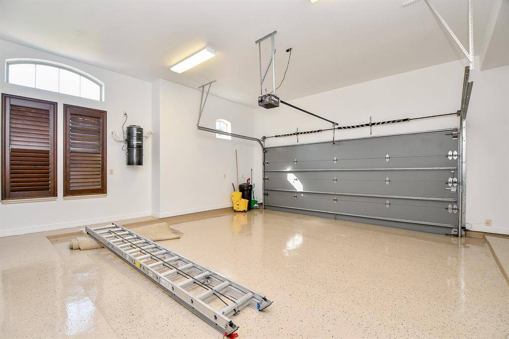 This is a clean, spacious garage with a high ceiling and ample lighting. It features an epoxy-coated floor, two windows with shutters, and an automatic door opener.