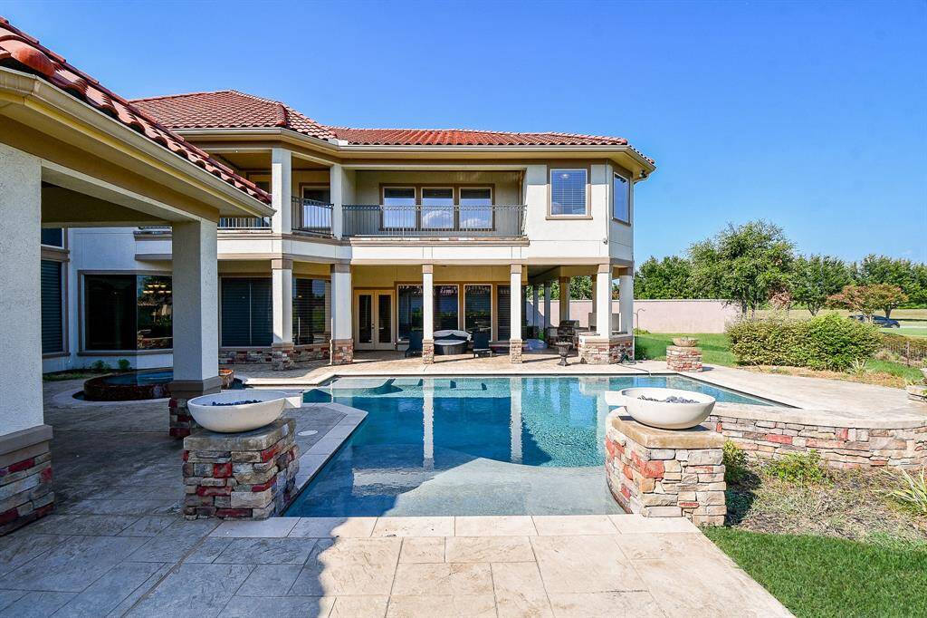 This is a luxurious two-story home featuring an elegant backyard with an in-ground pool, attached spa, and outdoor living spaces, set against a backdrop of a well-manicured lawn and open sky.