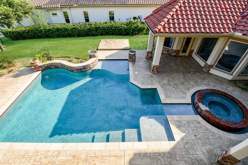 This property features a spacious backyard with a beautiful in-ground pool and an attached hot tub, complemented by a tiled patio area and a covered porch, ideal for outdoor living and entertainment.