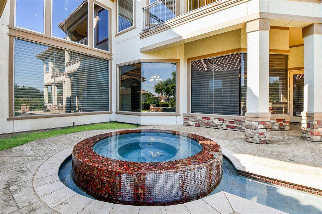 This home features a luxurious outdoor space with a mosaic-tiled spa, expansive windows, and a covered patio area, accentuated by elegant stone columns and a serene view, perfect for relaxation and entertainment.