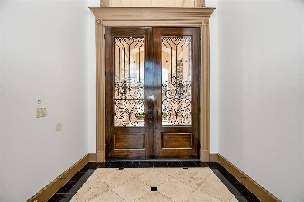 This is an elegant entryway featuring a beautiful wood door with intricate wrought iron details, complemented by a stylish tile floor design, creating a warm and inviting entrance to the home.