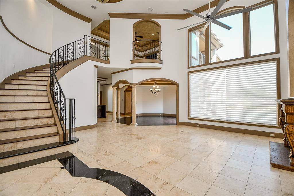 This is a spacious and elegant foyer featuring high ceilings, a grand staircase with wrought-iron railings, marble flooring, and an expansive window that floods the space with natural light. The open layout offers a view into adjoining rooms, enhancing the sense of space.
