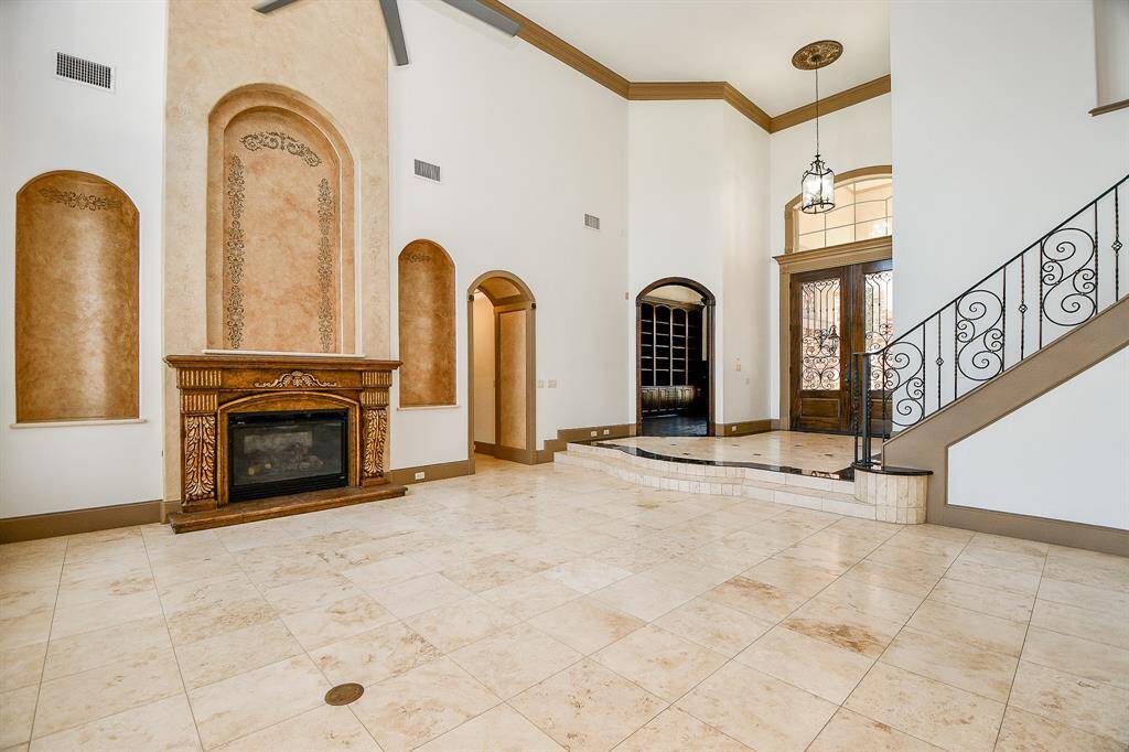 This is an elegant entryway with high ceilings, a grand staircase with wrought-iron railings, a decorative fireplace, and travertine flooring, leading to a welcoming arched front door.