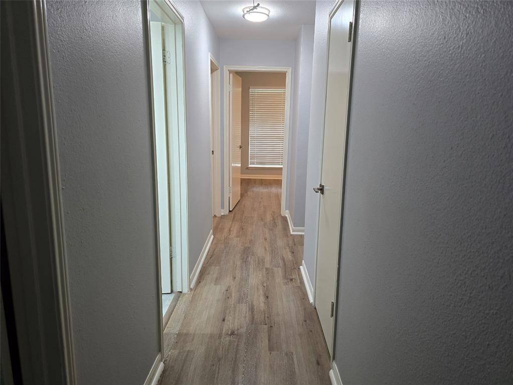 A modern hallway with new vinyl plank flooring, neutral gray walls, and white baseboard. It  links all four bedrooms which feature large new windows that flood the space with natural light.