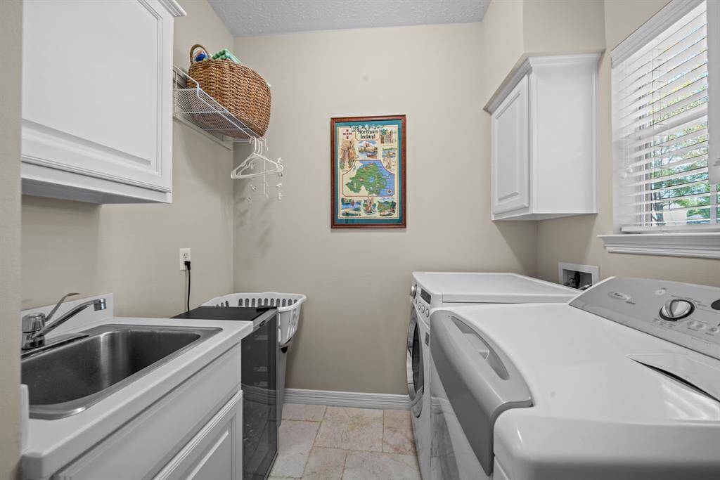 Laundry room with window overlooking the front yard, 2" blinds, cabinetry, a sink and space for a refrigerator.