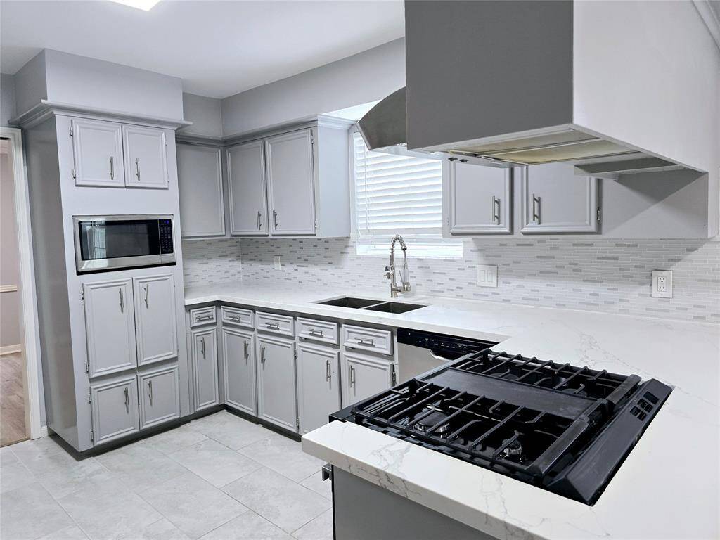 This updated and modern kitchen features gray cabinets, a built-in microwave, a gas stove, and a stylish tile backsplash. The space is bright and inviting, with ample counter space and contemporary fixtures.
