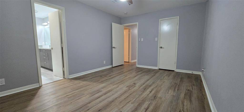The spacious, primary bedroom features fresh gray walls and new vinyl plank flooring. It includes an ensuite bathroom with modern fixtures and a practical layout.