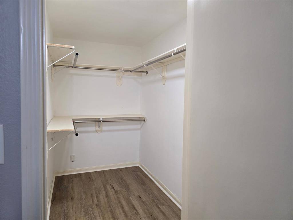 Spacious walk-in closet with new vinyl plank floors, multiple shelves, and hanging rods, offering ample storage.