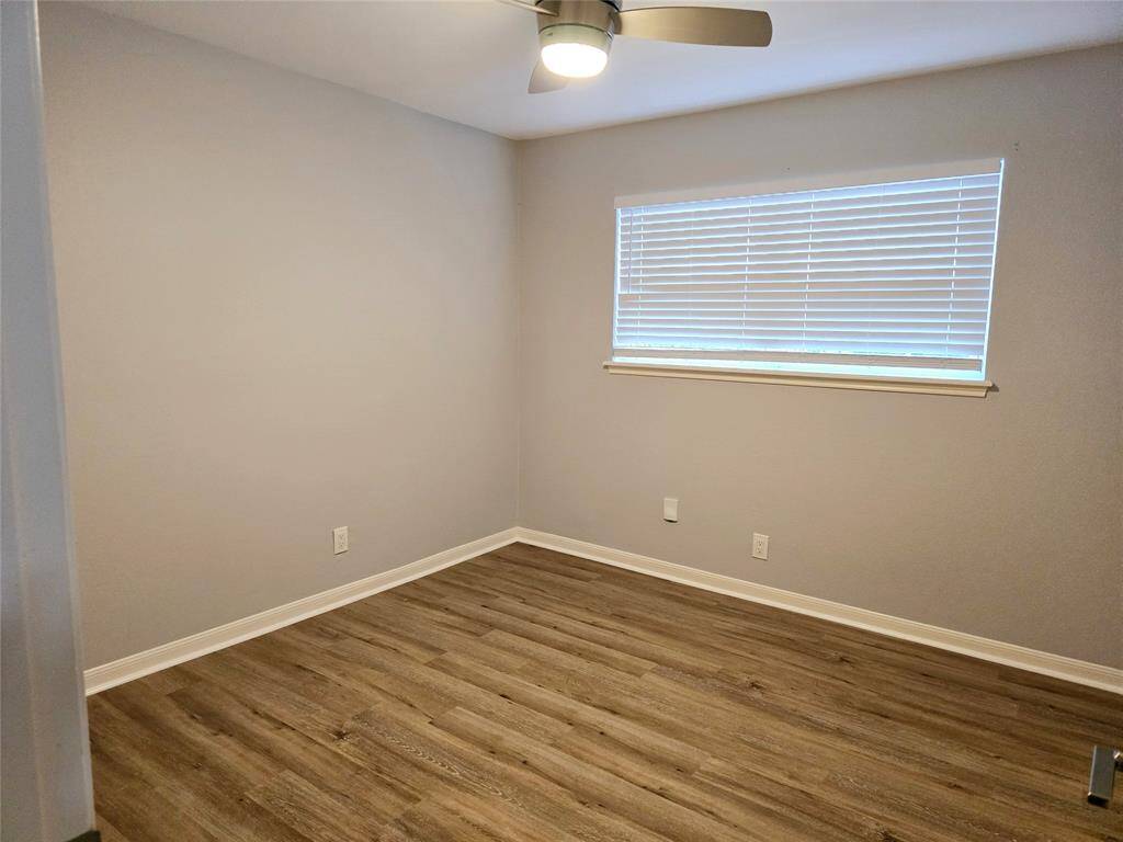 This fourth bedroom features fresh gray walls, wood-style flooring, a large new window with blinds, and a ceiling fan, offering a cozy and modern space.