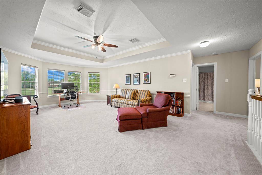 The spacious game room features plush carpet, tray ceilings with a ceiling fan, double crown molding, chair molding and a fierce view of the golf course!