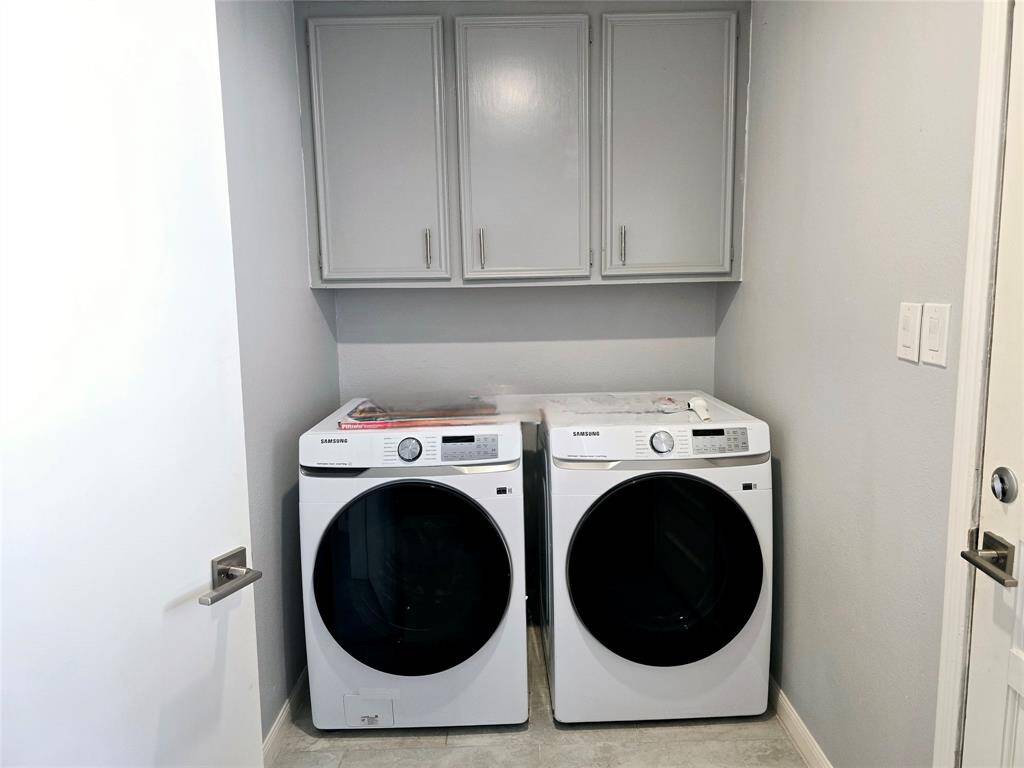 Functional and convenient in-house laundry room with new washer and dryer set, overhead storage cabinets, and a neutral color palette.