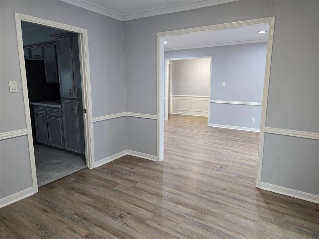 The formal dining room incudes light gray walls, white trim, and vinyl plank flooring. The space features crown molding and wainscoting, and it connects to the kitchen, formal living room and foyer, which provides great flow for entertaining.