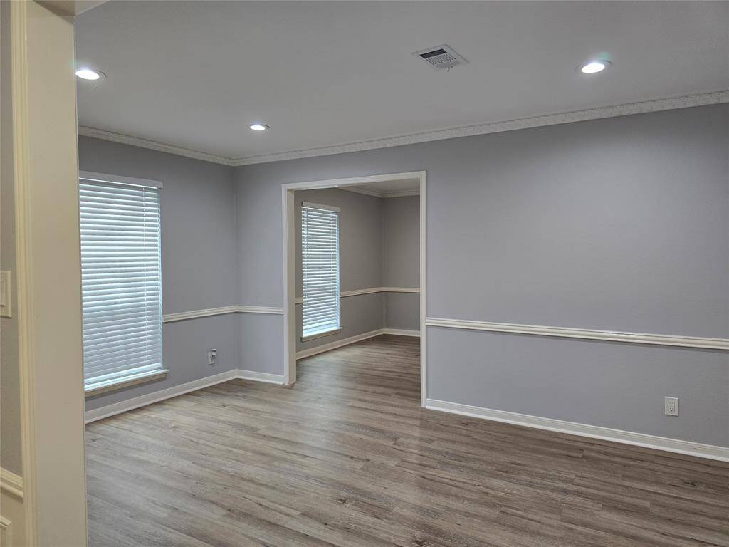 The formal living area features recessed lighting, a new large window with blinds, and an adjoining dining area visible through an open doorway. The room has a clean, modern feel with white trim accents.