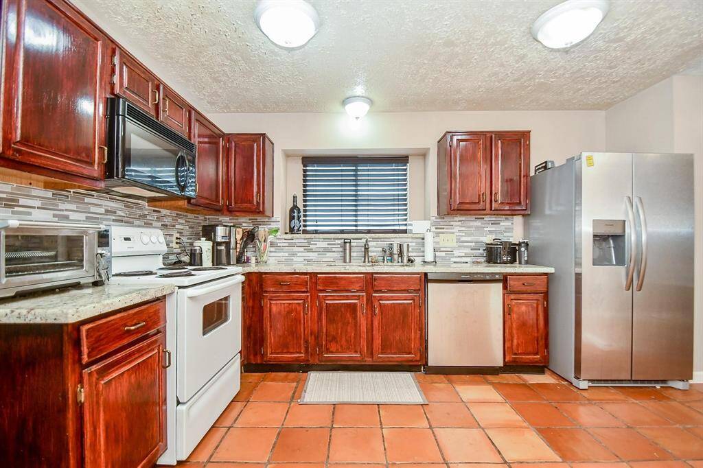 Spacious kitchen featuring terracotta tile flooring, rich wood cabinetry, granite countertops, and perfectly complemented by a stylish backsplash.