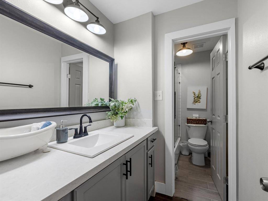 This bathroom features a modern design with a wide vanity, sleek fixtures, and ample counter space. It includes a large mirror, stylish lighting, and a separate toilet area, offering both functionality and a clean, contemporary look.