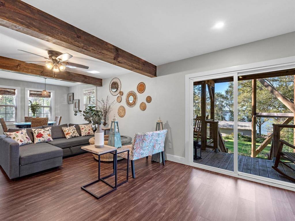 This inviting living space features a cozy sectional sofa, stylish decor, and warm wood accents. Large sliding glass doors open to a deck with serene views of trees and water, enhancing the natural light and offering a seamless indoor-outdoor experience. Perfect for relaxation and entertaining.