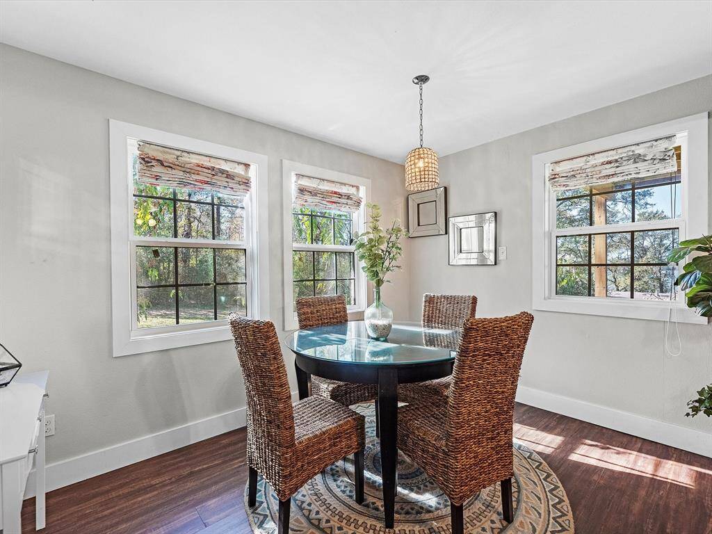 Bright and cozy dining area featuring a round glass table, wicker chairs, and large windows with a view of greenery. The space is accented by a stylish pendant light and neutral decor.