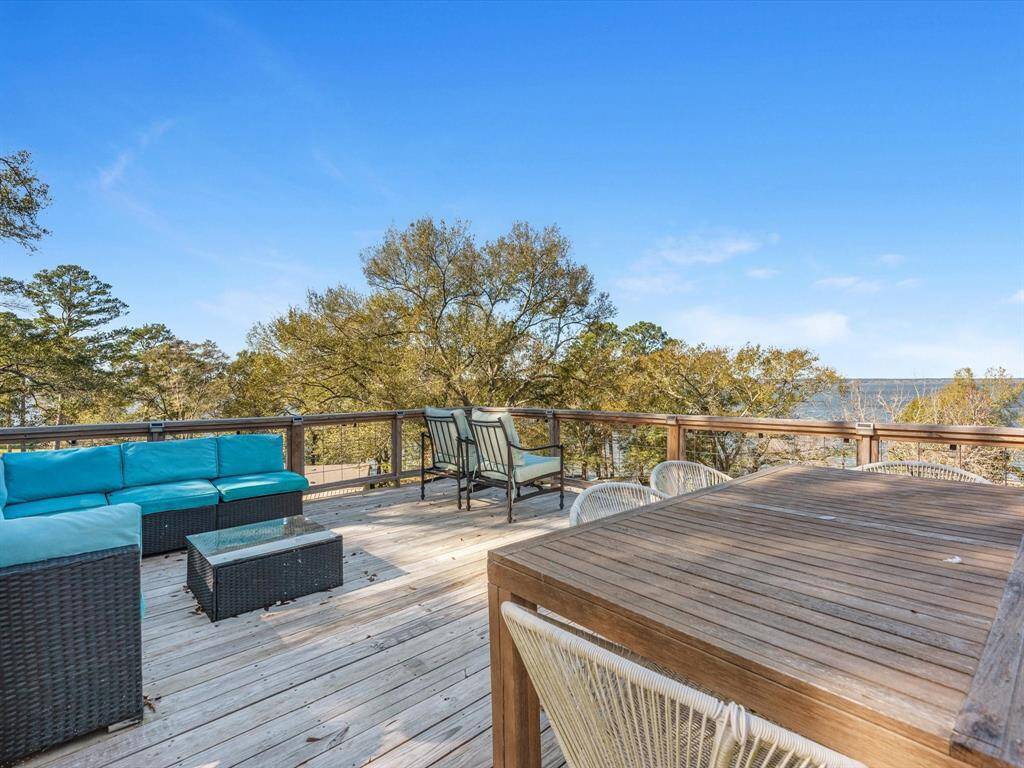 Spacious wooden deck with comfortable seating, offering scenic views of lush trees and a distant water body, perfect for outdoor relaxation and entertaining.