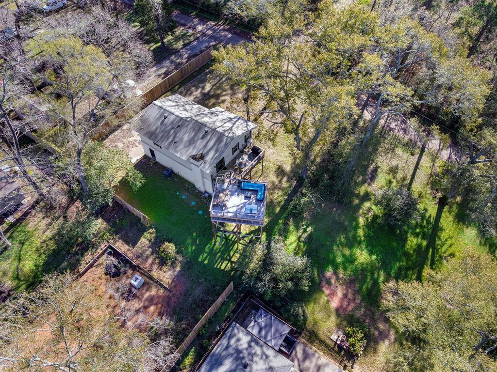 This aerial view showcases a charming home nestled in a spacious, wooded lot. The property features a large deck, providing a great outdoor space for relaxation or entertainment, surrounded by lush greenery and mature trees for privacy and a serene atmosphere.
