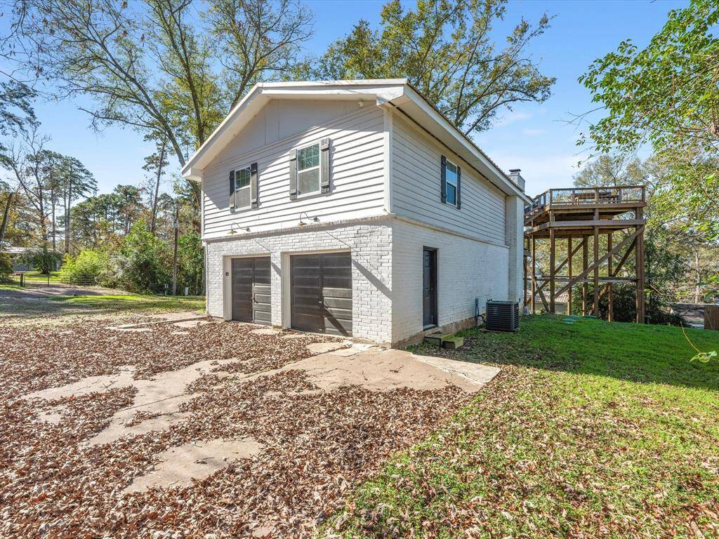 This home features a two-story design with a white brick and siding exterior. It includes a double garage, a spacious driveway, and a large elevated deck. Surrounded by trees, it offers ample outdoor space in a serene setting.