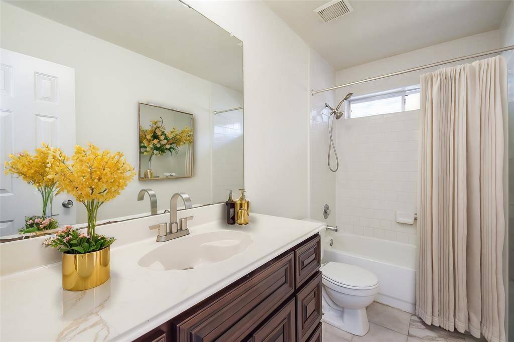 This spacious bathroom features a large mirror and a well-designed vanity area, providing ample surface space for daily routines. Additionally, it includes plentiful cabinets, allowing for efficient organization and storage of bathroom essentials.