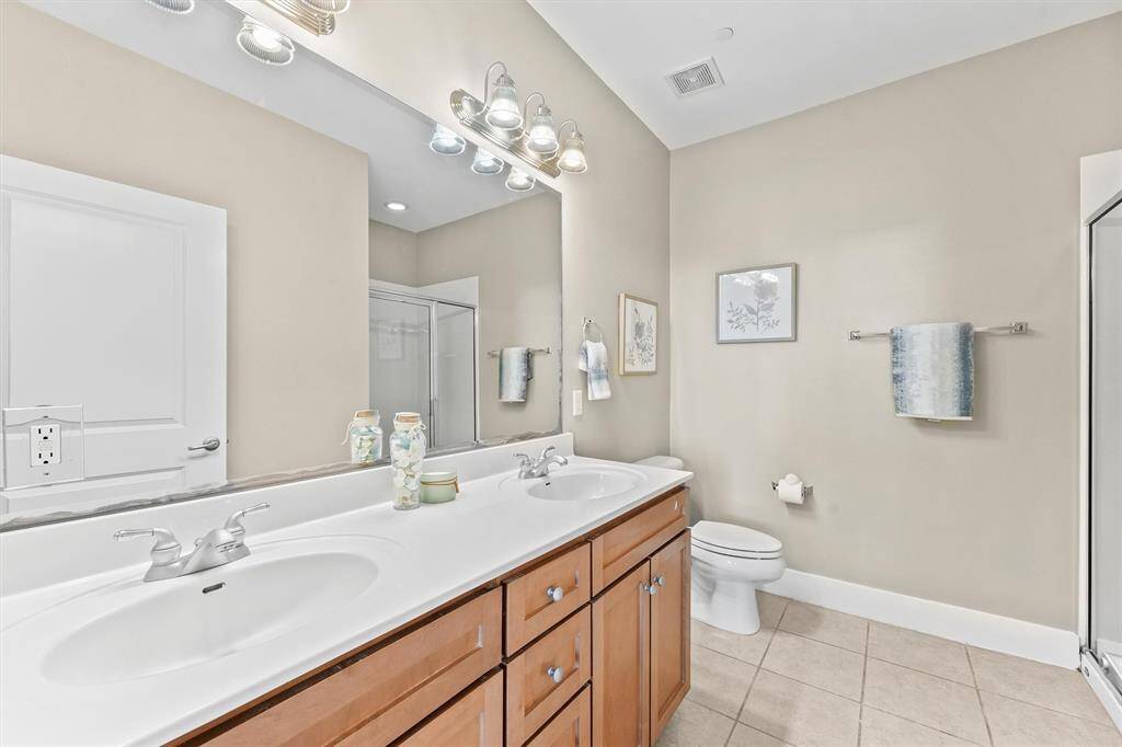 The primary bathroom features a spacious double vanity with ample counter space and under-sink storage. The large mirror and modern lighting fixtures provide excellent illumination, enhancing the room's functionality and style.