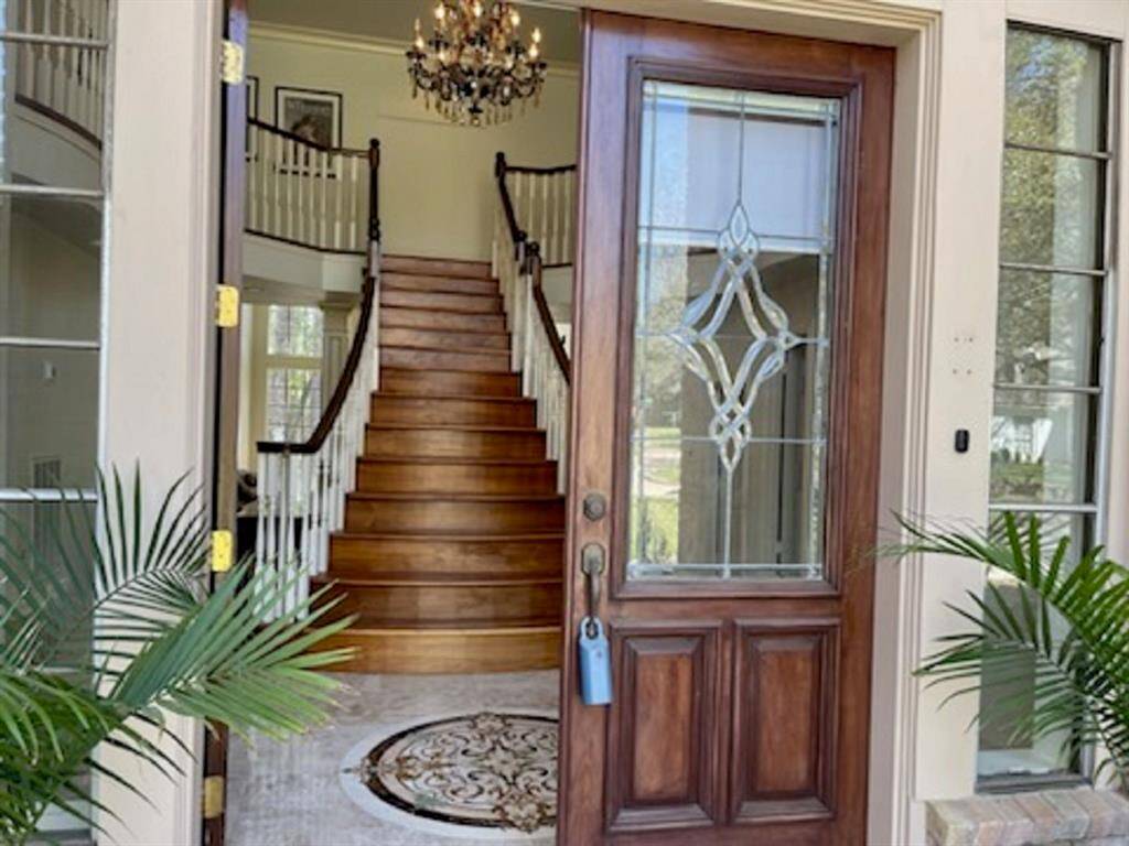 Welcome to this stunning home featuring an elegant staircase, a grand chandelier, and a beautifully crafted wooden door with ornate glasswork.