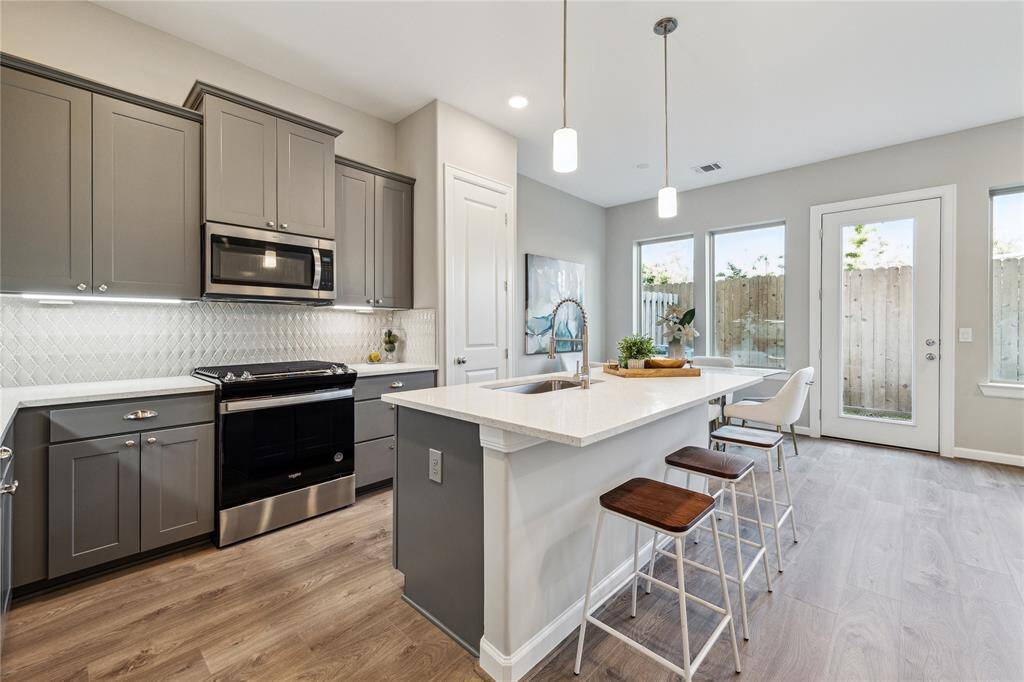 Kitchen has quartz seating island, stainless appliances including gas range, cabinet and pot drawers and pendant lighting.