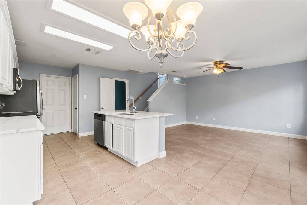 This kitchen features modern stainless steel appliances, a large center island with a sink, and white cabinetry. The space is brightened by natural light from a nearby window and an elegant chandelier, creating an inviting atmosphere.