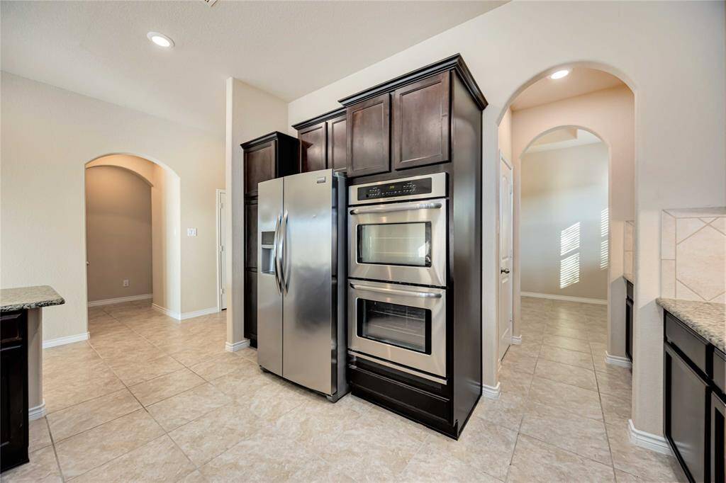 This kitchen features modern stainless steel appliances, including a double oven and refrigerator, surrounded by dark wood cabinetry. The space is bright and open, with tile flooring and arched doorways.