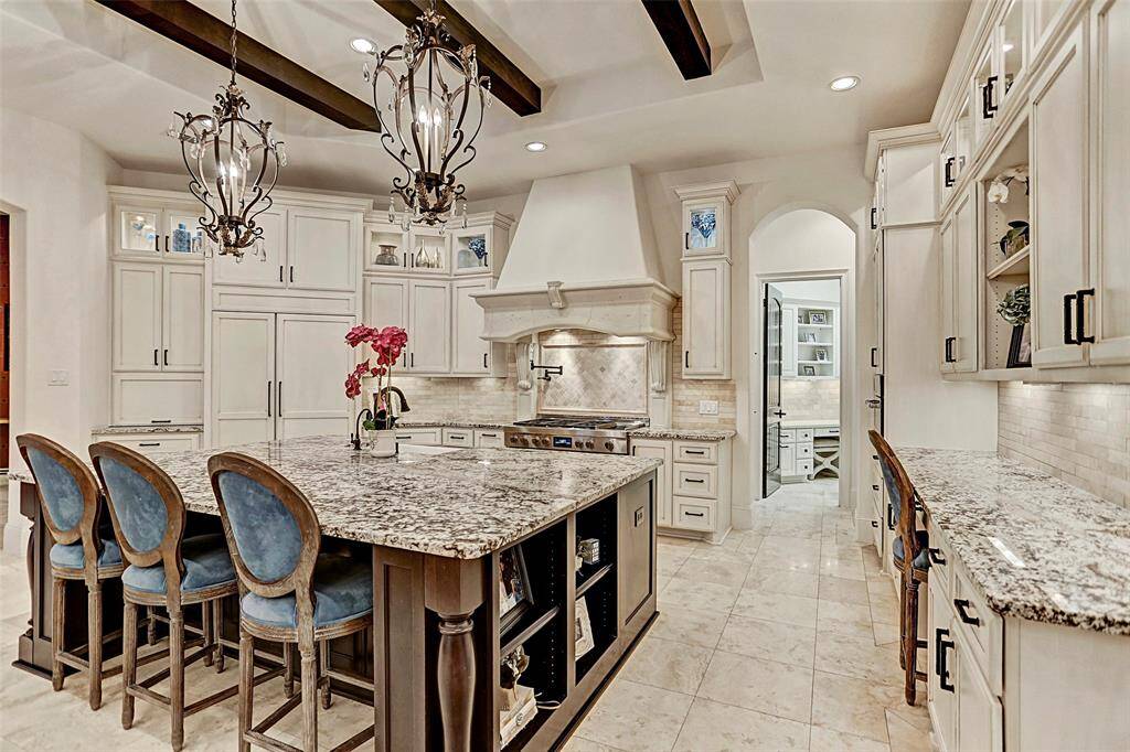 Gourmet Island Kitchen | This kitchen will impress daily with an oversized granite island, wood beamed ceiling, glass-front cabinets for showing off artwork, a built-in refrigerator and upgraded stainless steel appliances