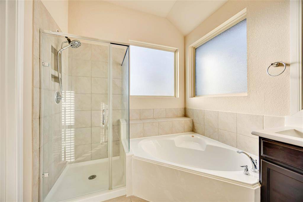 This bathroom features a modern design with a spacious glass-enclosed shower, a large soaking tub, and frosted windows for natural light and privacy.