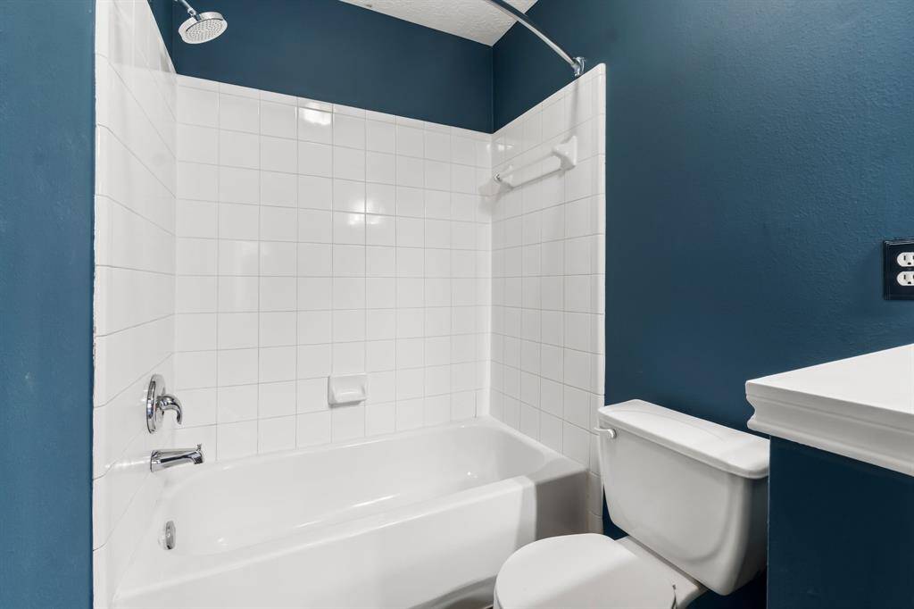 This bathroom features a clean, modern design with a white tiled shower and bathtub, complemented by dark blue walls. It includes a compact toilet and sink, creating a functional and stylish space.