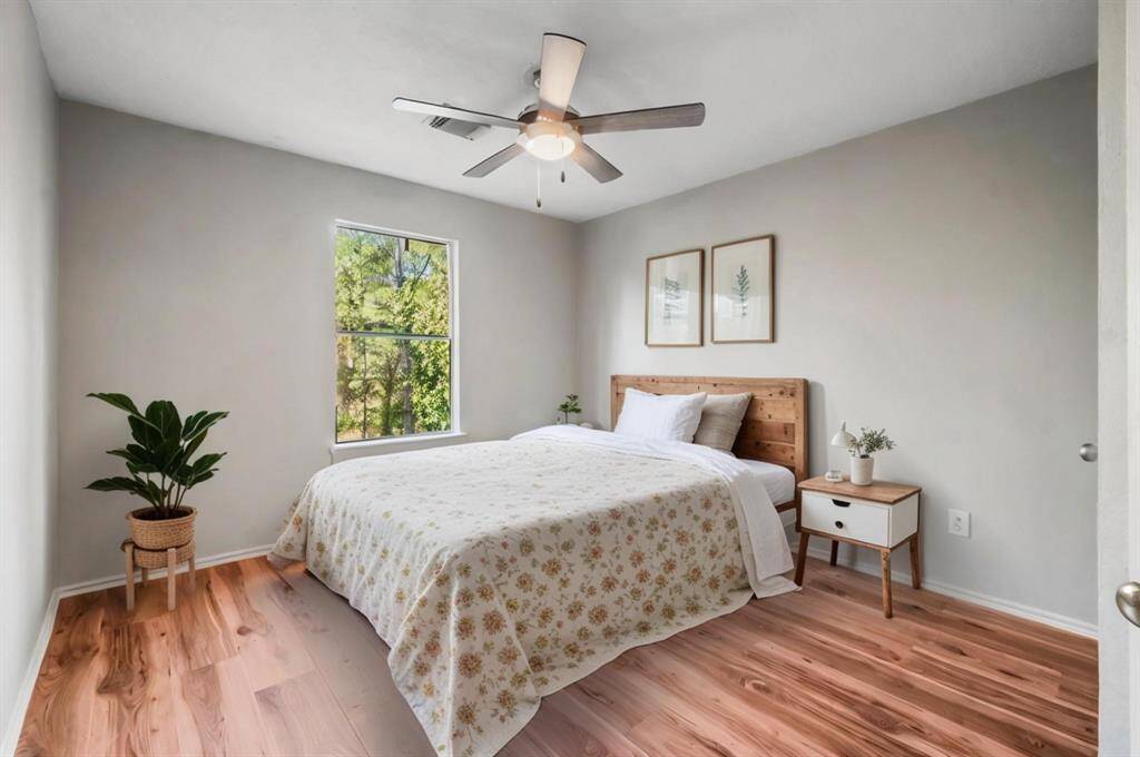This is a bright Secondary bedroom with light gray walls, wood flooring, a ceiling fan, and a window providing natural light and a view of greenery.