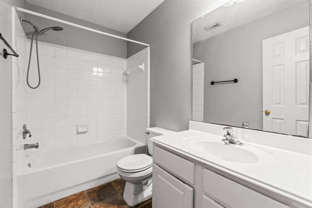 This Secondary bathroom features a clean, modern design with a white bathtub and shower, a large mirror above a white vanity, and neutral gray walls. The space is bright and functional, offering a sleek and inviting atmosphere.