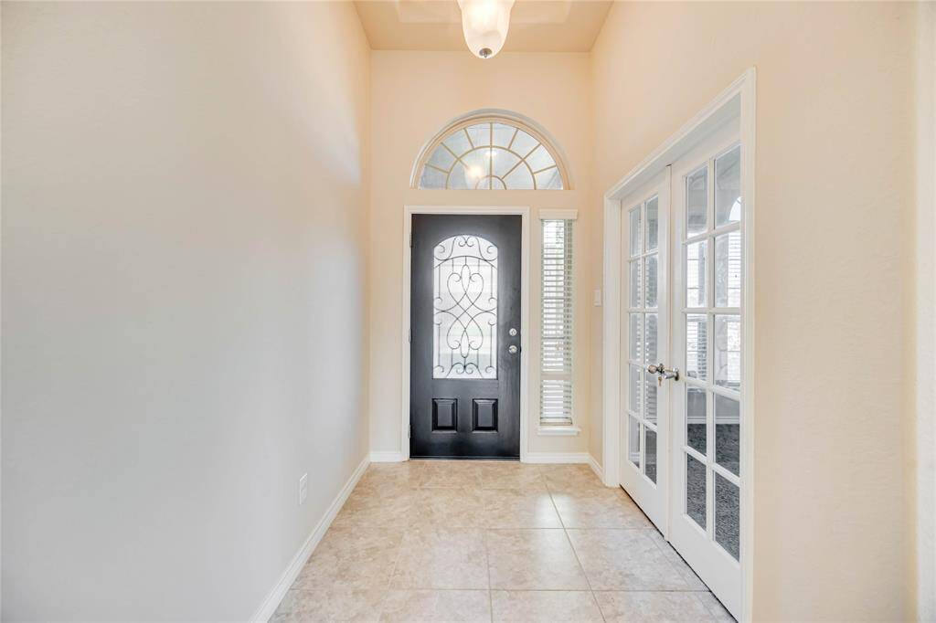 Bright entryway with a decorative black front door, tile flooring, and French doors leading to an study room.